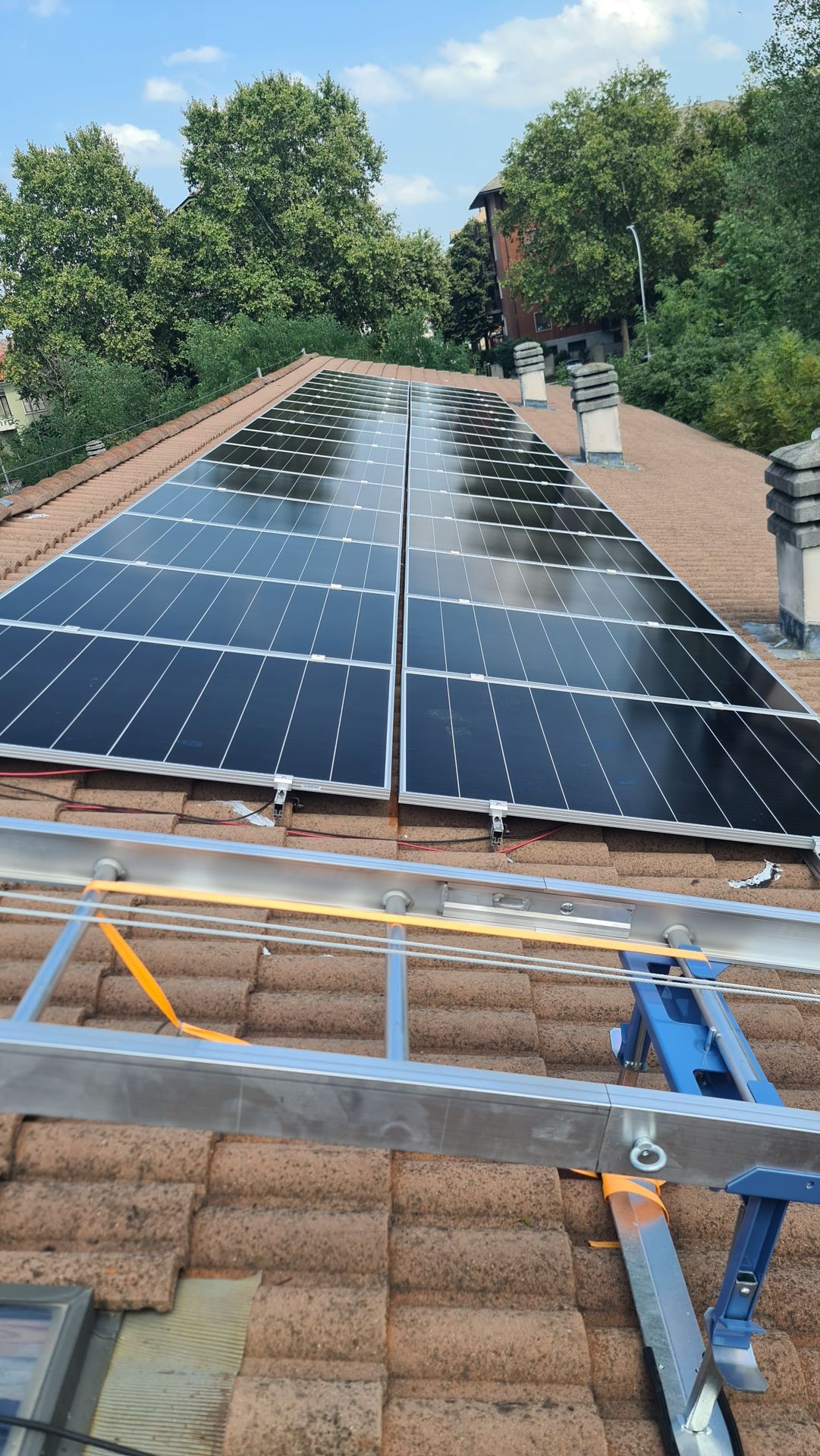 Rooftop with installed solar panels, surrounded by green trees and a clear blue sky above.